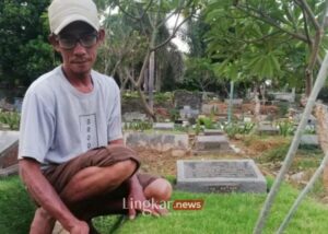 Seorang perawat makam menggunting rumput